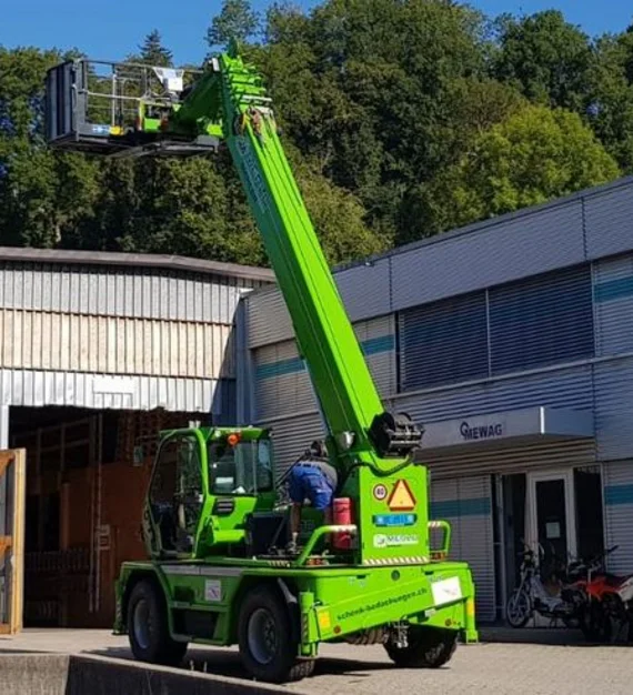 Teleskopstapler Merlo Ein grüner Merlo Teleskopstapler mit angehobener Arbeitsbühne vor Firmengebäude